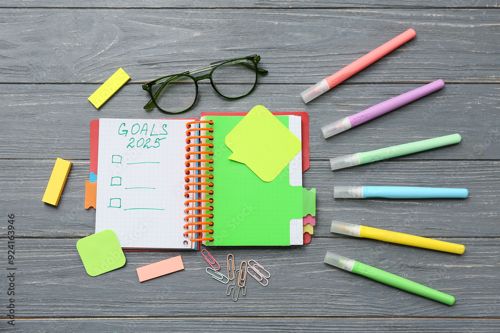 Notebook with to do list, stationery and sticky notes on black background. New year goals concept