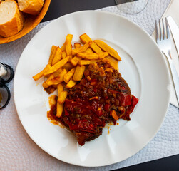 Wall Mural - Delicious oven roasted pork cheek topped with spicy vegetable salsa served with side dish of crispy french fries for dinner. Traditional Spanish dish