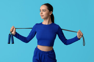 Wall Mural - Young female trainer with skipping rope on blue background