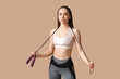 © Pixel-Shot - Young female trainer with skipping rope on beige background