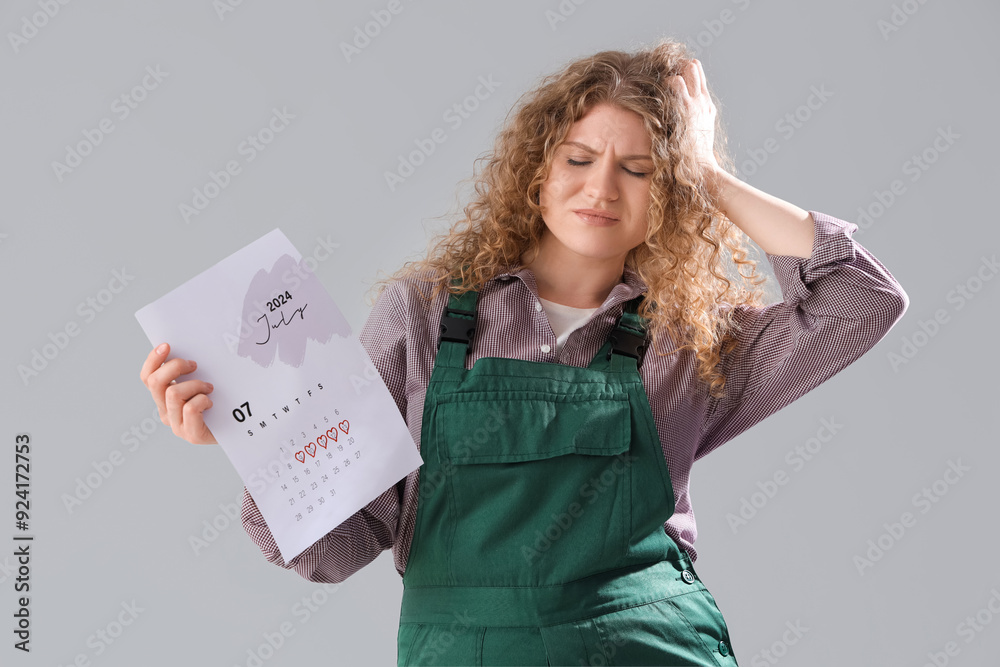 Female worker with menstrual calendar suffering from headache on grey background