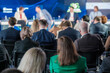 © Anton Gvozdikov - Audience members are attentively listening to a panel discussion at a business conference, focusing on various topics presented by speakers on stage.