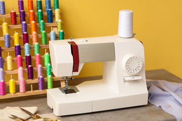 Wall Mural - Modern sewing machine with set of colorful threads and tailor's supplies on yellow background