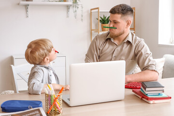 Poster - Young man and his little son having fun while doing homework in room