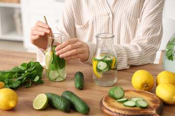 Wall Mural - Young woman and bottles of infused water with lemon, cucumber and mint on table in kitchen