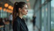 © umut hasanoglu - Young woman in a business suit stands by a window in a modern office setting, deep in thought.
