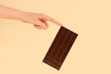 Wall Mural - Female hand with sweet chocolate bar on yellow background