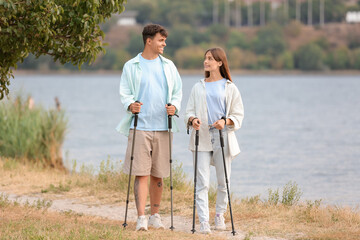 Canvas Print - Young couple training with walking poles near lake