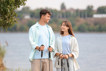 Canvas Print - Young couple training with walking poles near lake