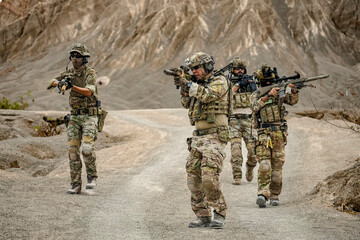 A group of military men in combat gear patrol in the middle of a desert and tropical jungle. Soldiers in full combat gear in dry weather conditions assemble and march on a mission.