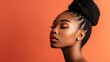 © Iswanto - Close-up portrait of a beautiful young African American woman with long braids and  glowing skin, against a bright coral background. She is looking down and has her eyes closed.