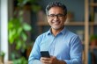 © Dream Canvas - Smiling mature Latin or Indian businessman holding smartphone in office. Middle aged manager using cell phone mobile app. Digital technology application and solutions, Generative AI