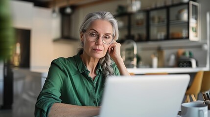 Wall Mural - A middle-aged woman is sitting at her desk, working on the laptop