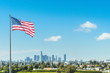 Against the backdrop of a city skyline with many high-rise buildings in the distance A close-up of the American flag fluttering in the blue sky. Naturalization, American dream, Freedom, patriotism. 