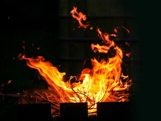 A fire is burning in a pile of wood. The fire is orange and yellow, and it is very hot. Dark black background. Barbeque into the night concept.