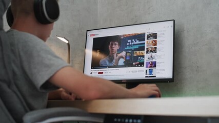 Poster - caucasian teenager in headphones watches educational blog about filmmaking on personal computer at h
