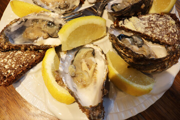 seafood and white wine in a glass. plate with oysters, lemon and bread with butter on a wooden table