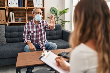 Sticker - At psychology clinic, elderly man in medical mask defiantly raises hand in serious 'stop' sign, confidently facing the danger of covid