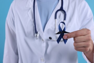 Wall Mural - Prostate cancer awareness. Doctor holding blue ribbon with fake mustache on color background, closeup