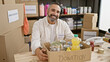 © Krakenimages.com - Smiling mature hispanic man with beard volunteering in a donation center, holding a box with canned food.