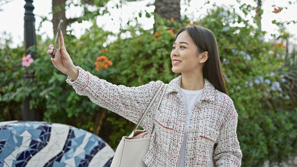 Canvas Print - An asian woman takes a selfie in a vibrant city park surrounded by lush greenery.