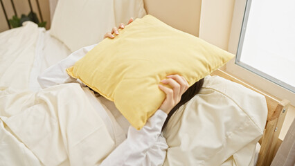 Canvas Print - Young asian woman hiding face with pillow in bright bedroom setting