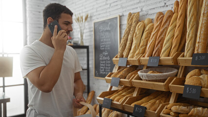 handsome young hispanic man talking on phone while shopping in bakery filled with various bread loav