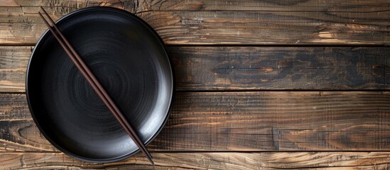 Poster - Japanese black plate and chopsticks resting on a wooden surface with a blank area ideal for display in a photograph. Creative banner. Copyspace image