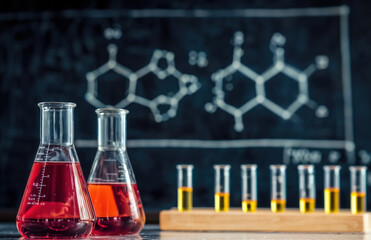 Poster - Glassware red and yellow liquid in a laboratory with a blackboard chemical formulas in the background