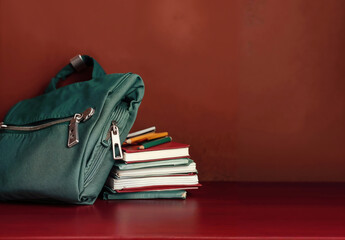 Aufkleber - Green backpack on stack of books and pencils on red table and red wall background with copy space for back to school