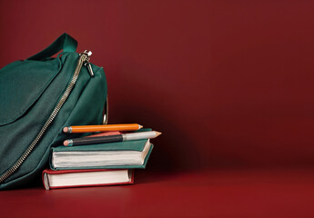 Aufkleber - Green backpack standing near stack of books and pencils on red background with copy space