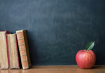 Poster - Table with a red apple and old books in front of a blank blackboard, copy space background