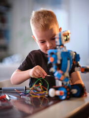 A young boy focused on assembling a colorful robot with various wires at play, capturing a moment of concentration and creativity in a well-lit indoor setting.