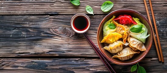 Sticker - Wooden background with a bowl of colorful dumplings accompanied by soy sauce cabbage and chopsticks leaving room for text in the copy space image