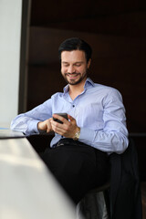 Wall Mural - A man is sitting at a table with a cell phone in his hand. He is smiling and he is enjoying himself