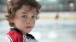 © nopommajun - A young boy with curly hair standing on an ice rink, wearing a hockey jersey, looking directly at the camera.