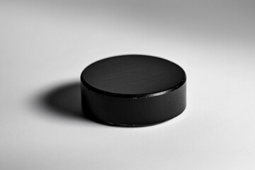 Wall Mural - Black hockey puck on white background, shadow stretching behind. Minimalist sport essence, simple equipment. Stark contrast, circular shape. Ideal for sports, competition, winter themes