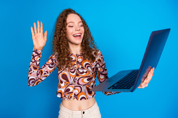 Poster - Photo portrait of pretty young girl hold netbook video call wave hand hi wear trendy colorful outfit isolated on blue color background