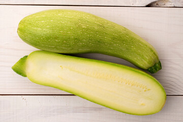 One whole and one half ripe zucchini on a wooden table, macro, top view.