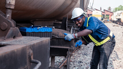 Wall Mural - African machine engineer technician wearing a helmet, groves and safety vest is using a wrench to repair the train