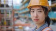 © nopommajun - A female construction worker wearing a safety helmet and reflective vest stands at a construction site with a determined expression.