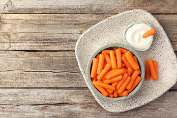 Sticker - Baby carrots in bowl and sauce on wooden table, top view. Space for text