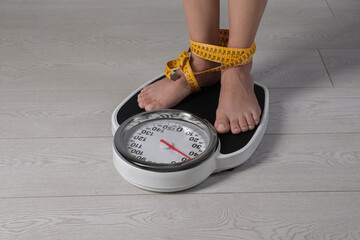 Poster - Eating disorder. Woman tied with measuring tape standing on floor scale indoors, closeup