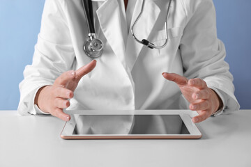 Poster - Doctor with tablet at table against light blue background, closeup view