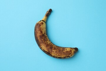 Canvas Print - Overripe banana with dark spots on light blue background, top view