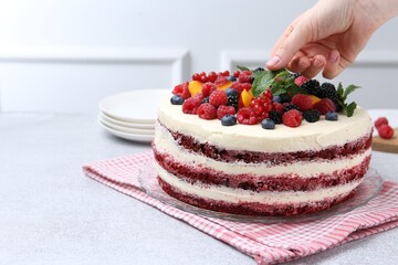 Wall Mural - Woman decorating tasty sponge cake with mint at light grey table, closeup