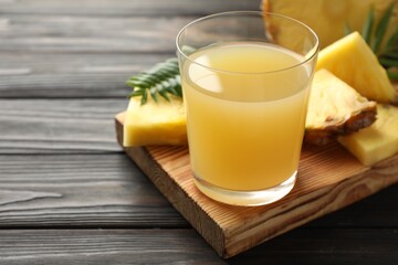 Tasty pineapple juice in glass and slices of fresh fruit on wooden table, closeup. Space for text