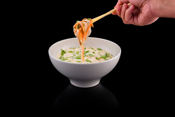 Hand lifting noodles with chopsticks from soup bowl