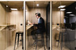 © ADDICTIVE STOCK CORE - An executive engrossed in work uses headphones in a soundproof booth, ensuring privacy and concentration in a modern office