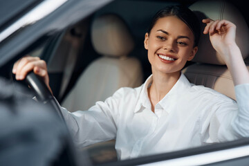 Woman driving car, smiling as she sits with her hand on the steering wheel and head tilted toward the camera, capturing a moment of joy and ease